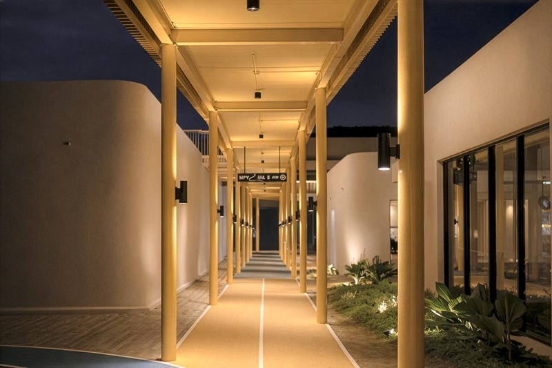 Covered timber colonnade with white cylindrical volumes and planted courtyard at night