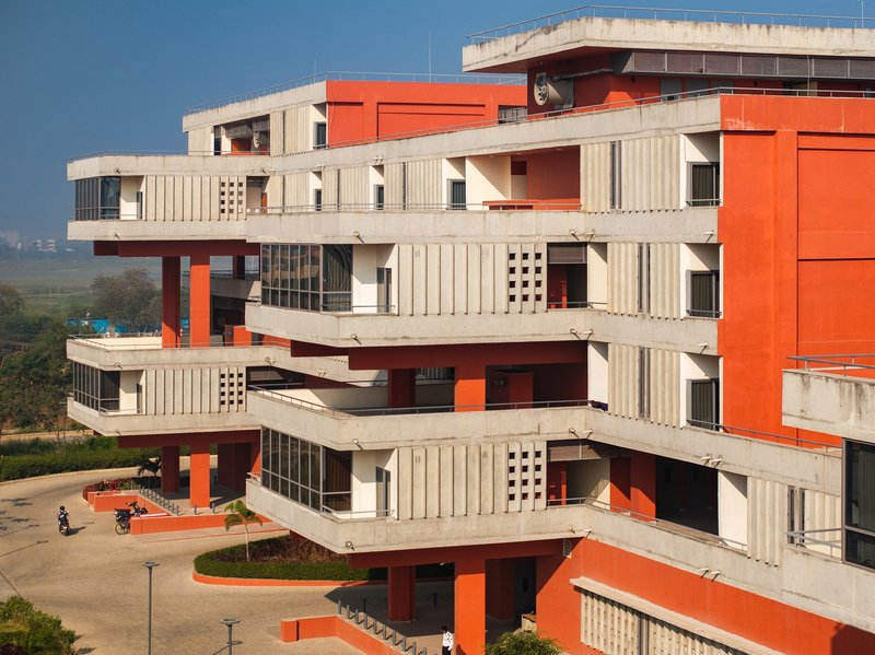 Three-quarter view of the stepped concrete balconies and red structure