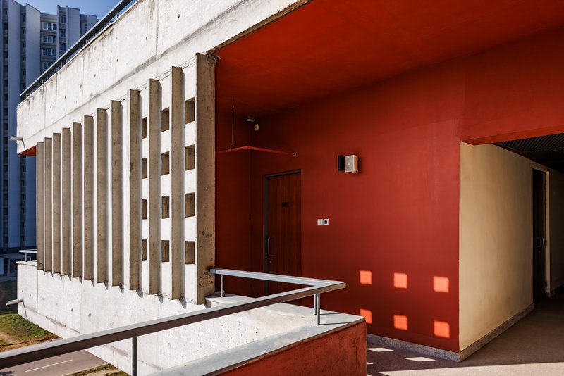 Concrete brise-soleil screen wall meeting a red-painted wall at a doorway