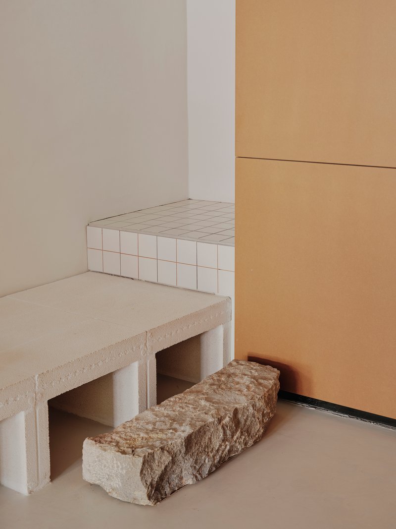 Corner detail showing white tiled bench with raw stone blocks on pale flooring beside timber panels