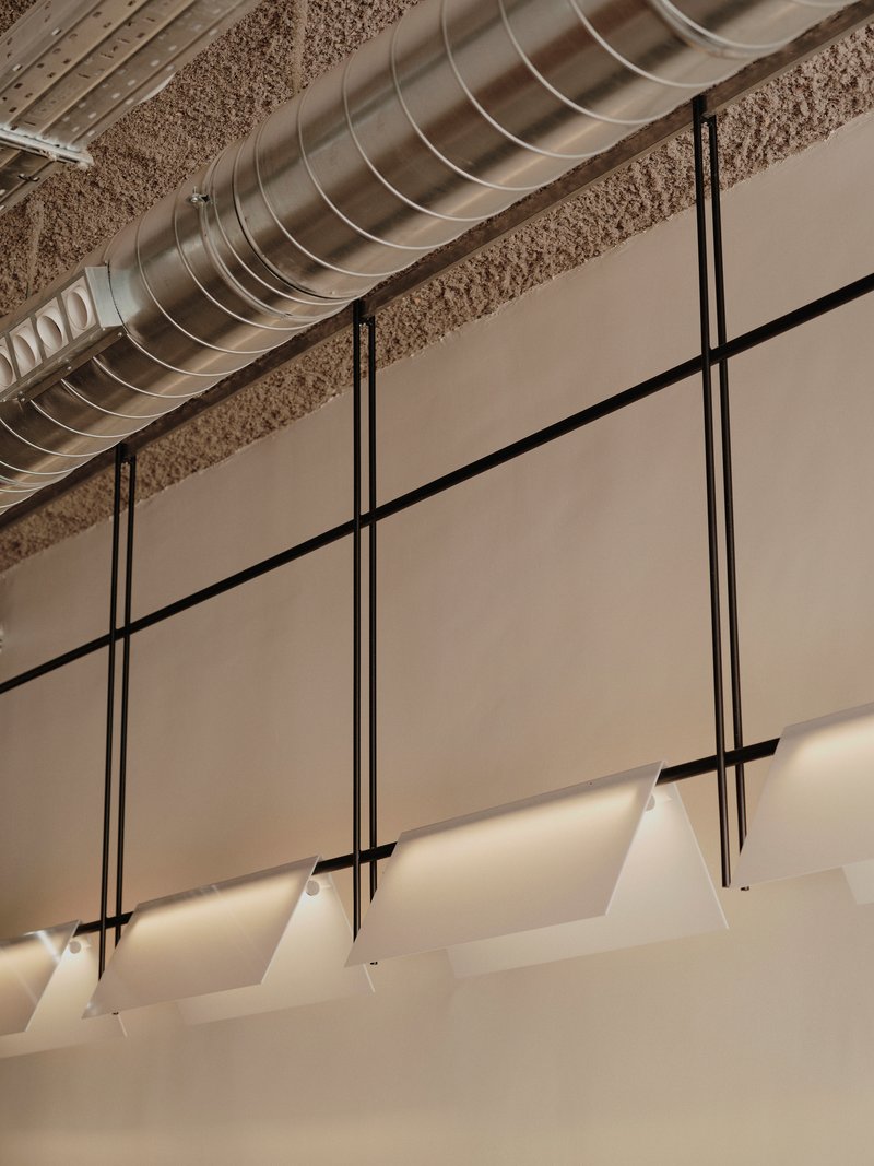 Exposed spiral ductwork running above suspended pendant lights on black cord against textured ceiling