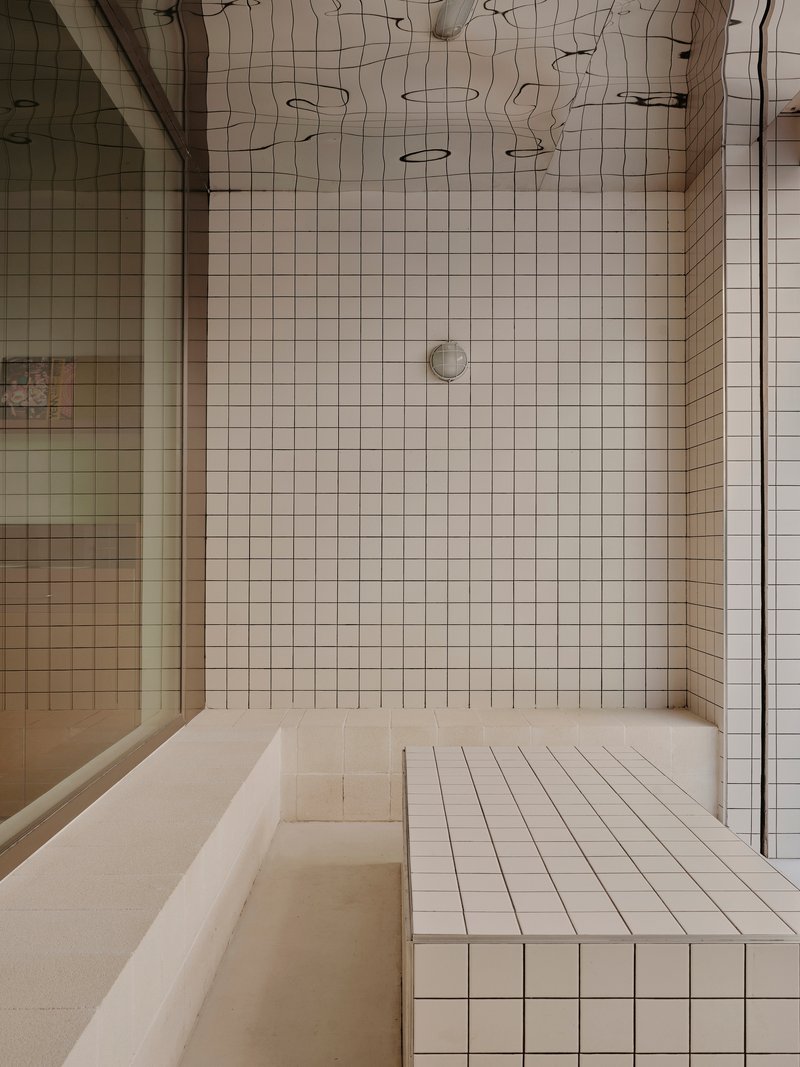 Tiled shower enclosure with built-in bench and white grid ceramic walls beneath exposed ceiling joinery
