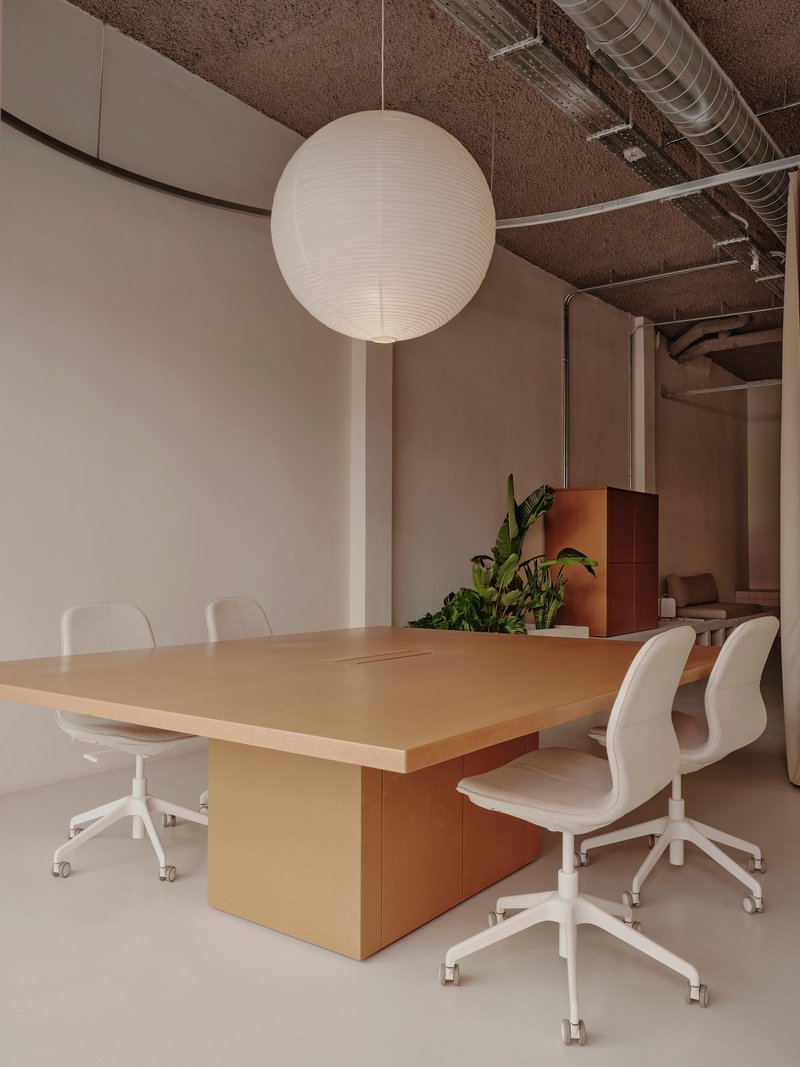 Conference table with timber pedestal base beneath a sphere pendant and exposed textured ceiling with ventilation ductwork