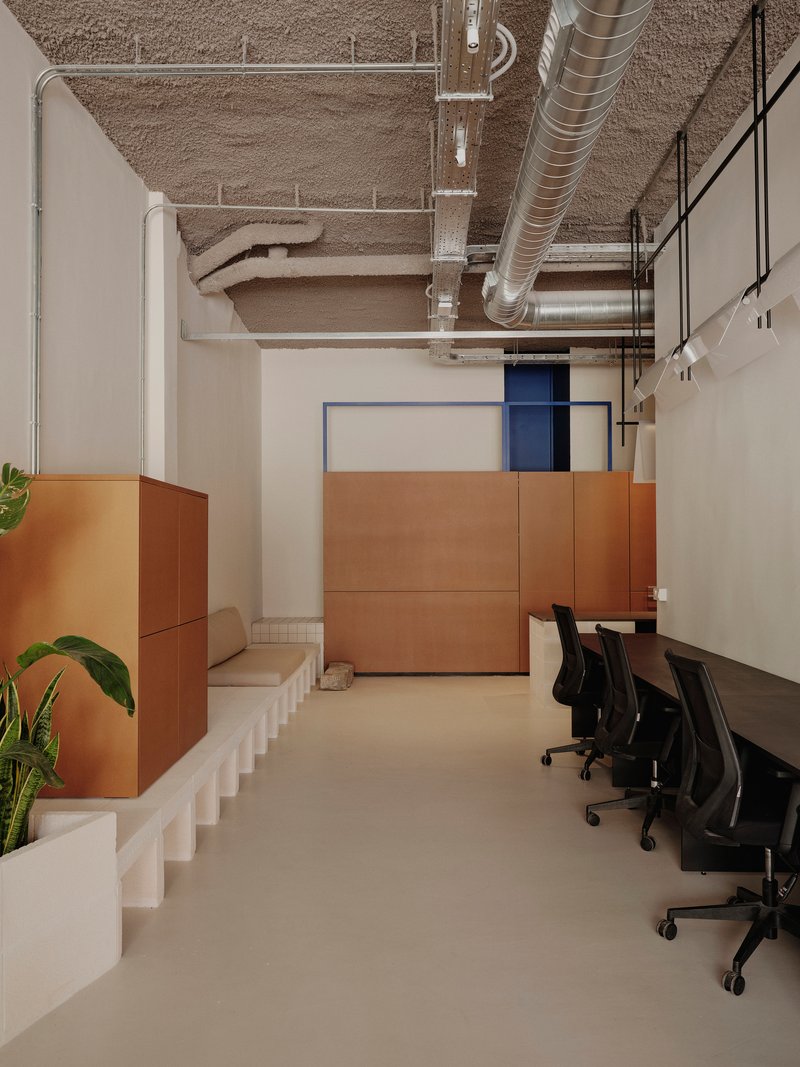 Office space showing copper-clad joinery elements, white stepped seating platform, and exposed concrete ceiling with metal ducts