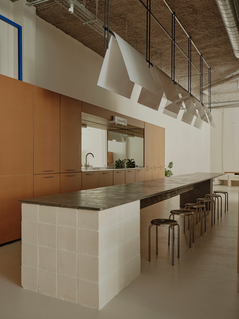 Island table with white concrete block base and timber cabinetry beyond in a space with exposed ductwork