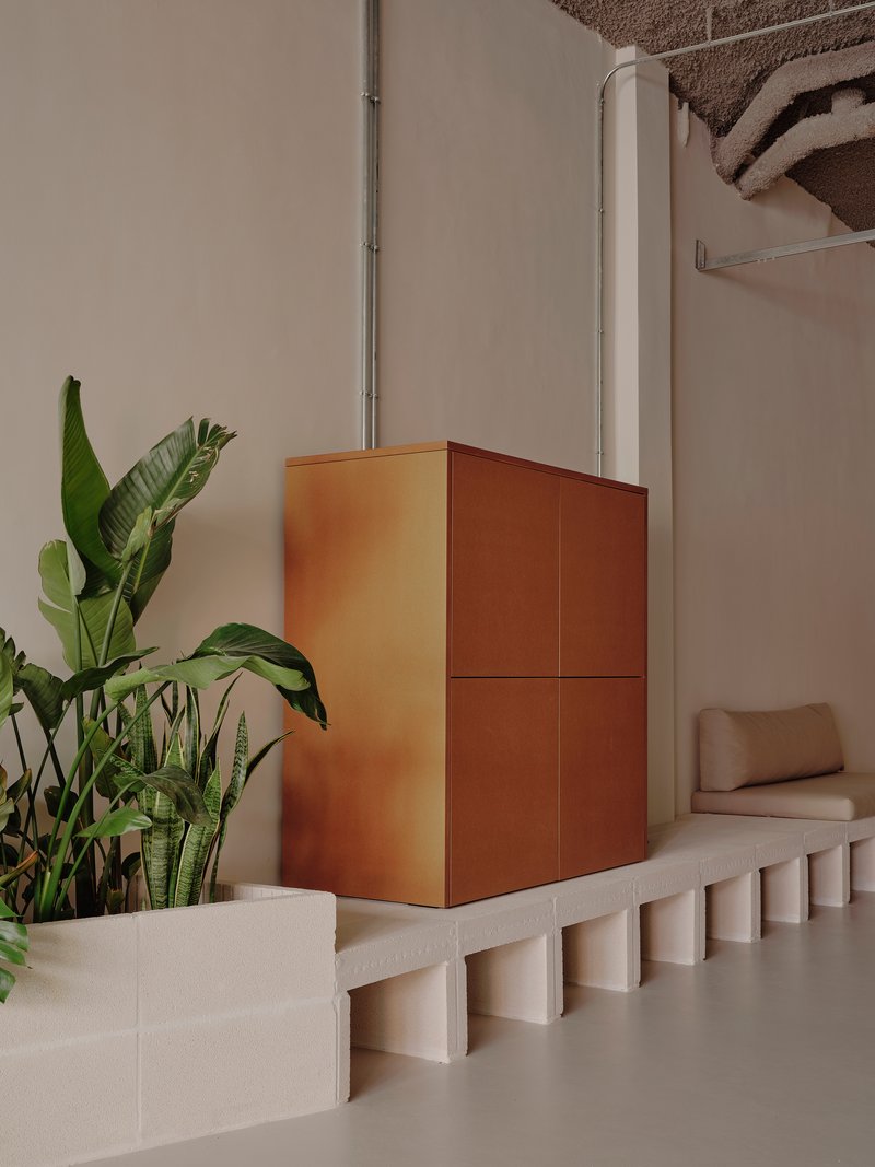 Copper-clad cubic volume on a fluted concrete plinth beside tropical plants and a white column