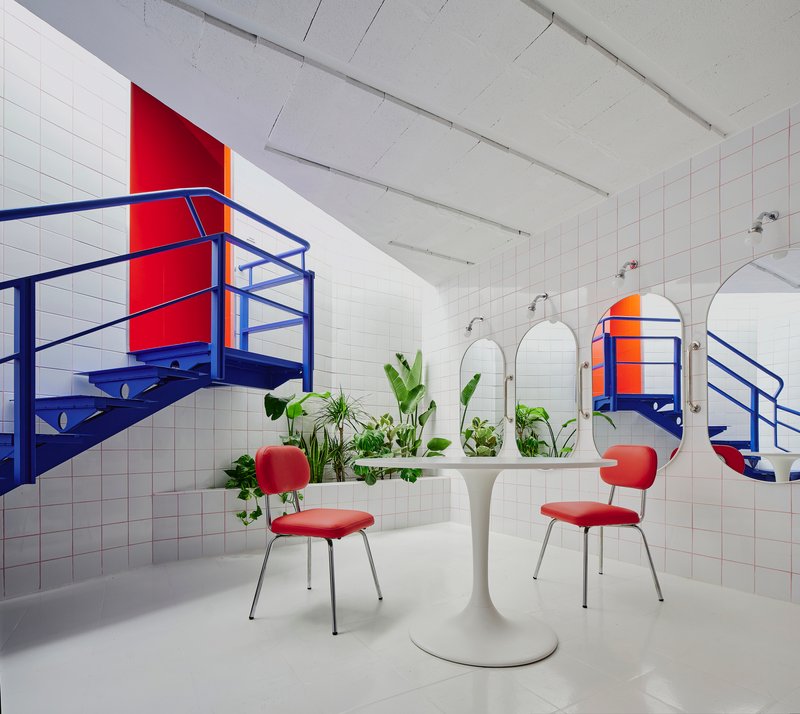 White tiled room with blue steel staircases, red accent panels, round mirrors and potted greenery