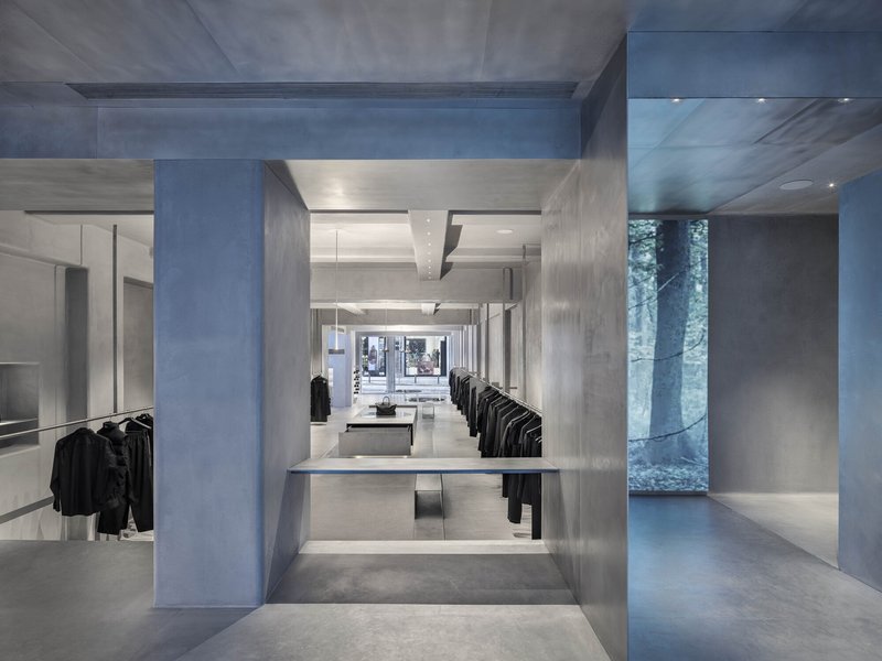 Long interior view through concrete portal showing recessed display tables and clothing racks