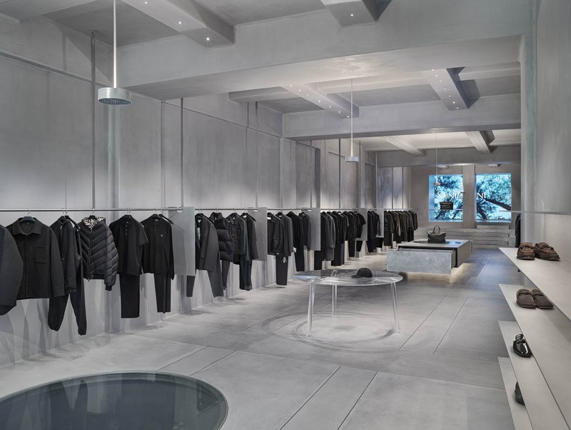 Retail floor with clothing racks on glass dividers, circular floor openings and windows overlooking trees
