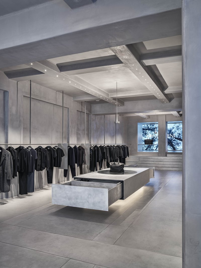 Concrete coffered ceiling with recessed lighting above clothing display and windows overlooking trees