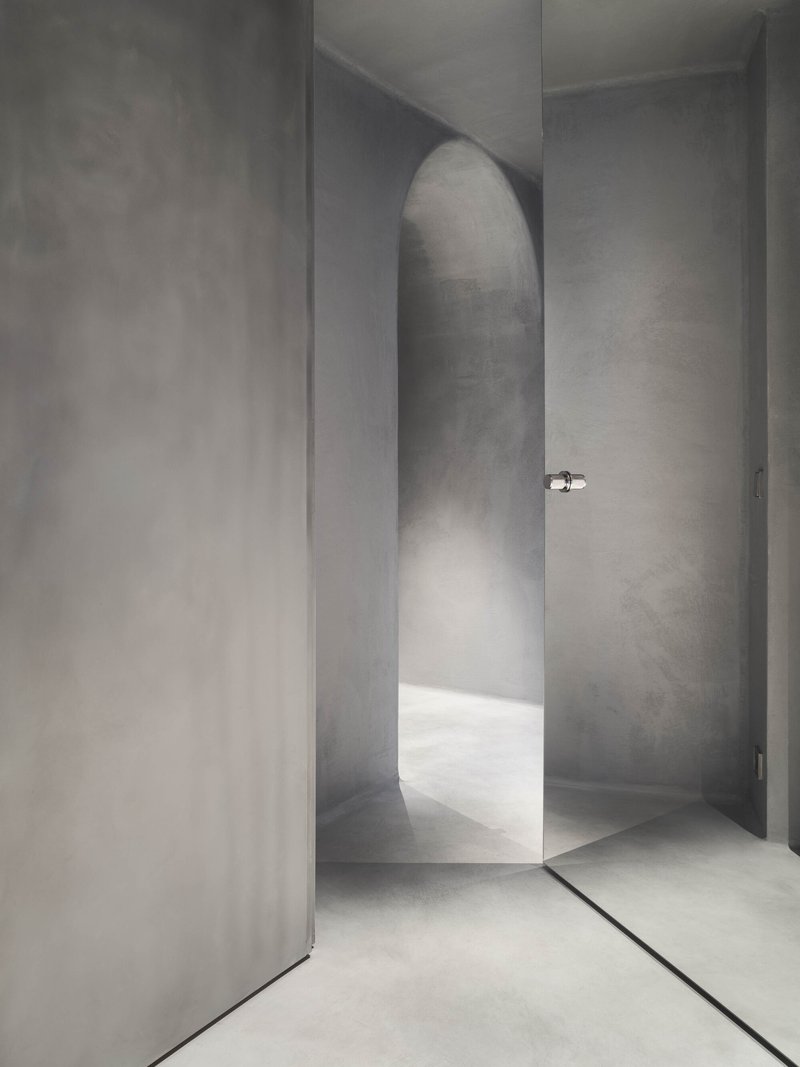 Arched passageway in smooth plaster with chrome door handle and soft natural light
