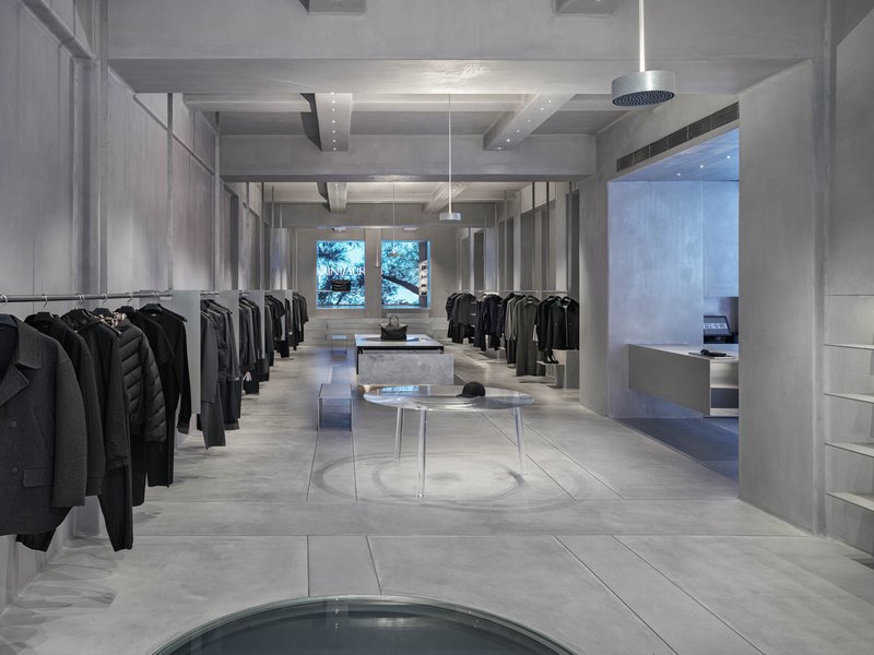 Interior retail space with exposed concrete beams, clothing racks and circular floor inset under pendant lighting