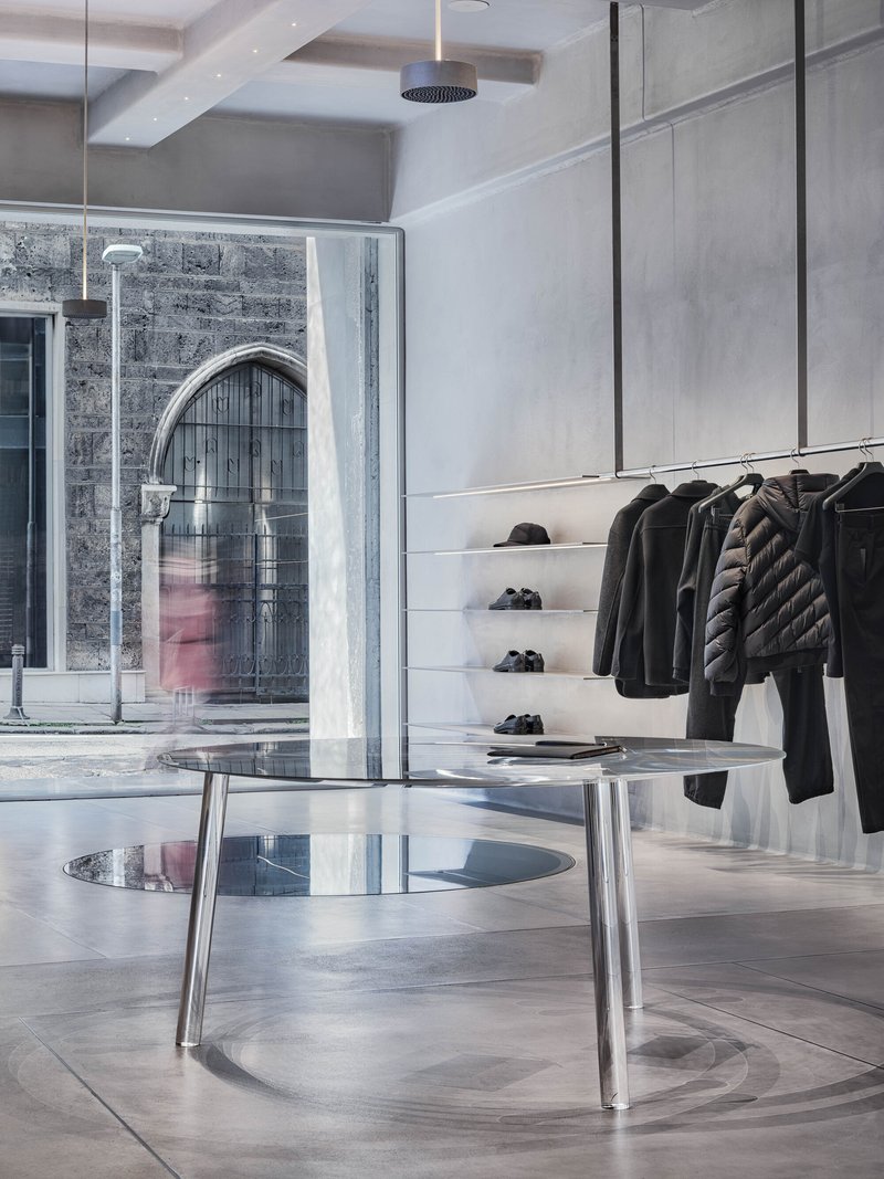 Glass storefront revealing an arched brick facade with a person passing in pink clothing