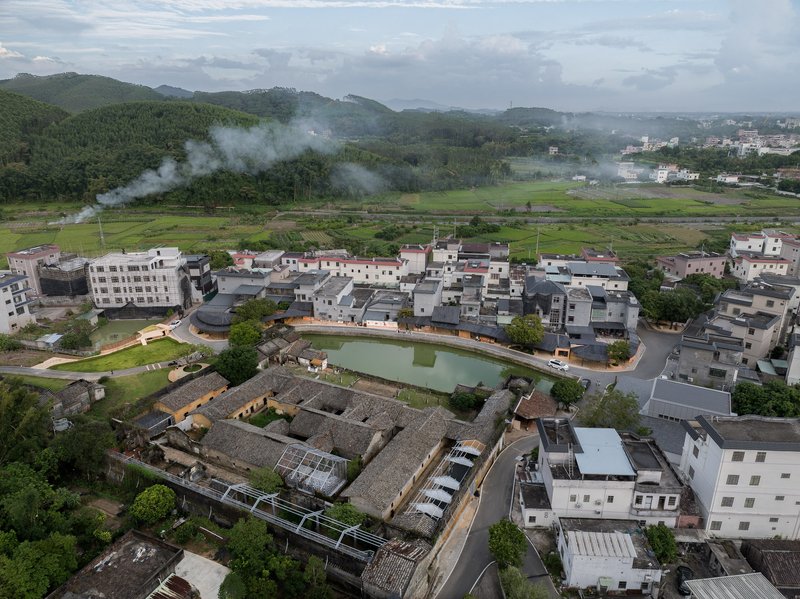 Aerial view of a village with tiled roofs surrounding a central pond and green fields in mist