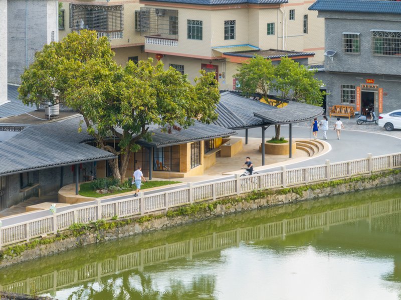 Curved tile roofs along a pond with white balustrade and pedestrians crossing the paved plaza