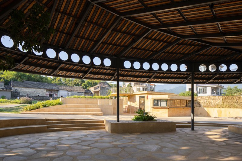 Covered pavilion with timber slat ceiling, steel columns and circular roof openings framing afternoon light