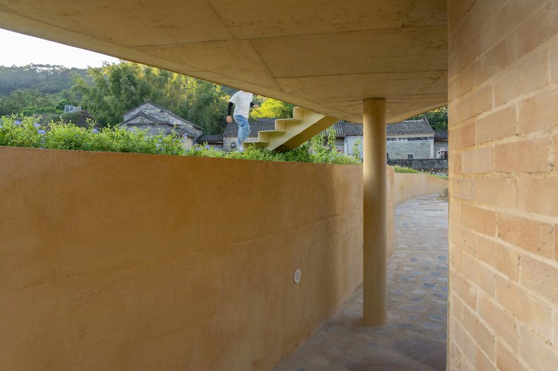 Passage between rammed earth walls and cylindrical column beneath the angled timber soffit