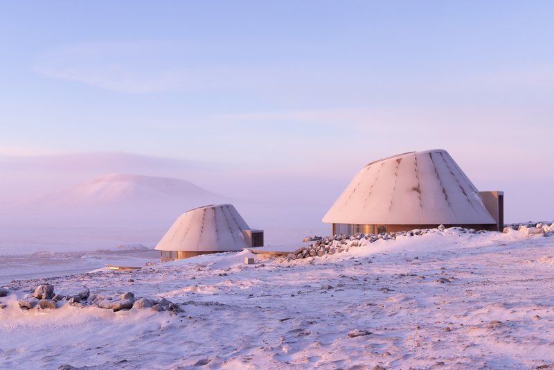 Two dome shelters with illuminated glazed entries on a rocky snowfield at twilight