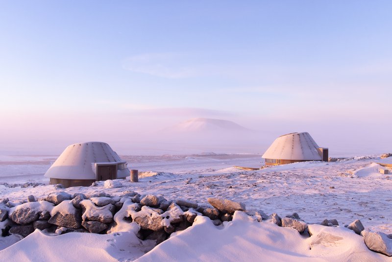 Pair of dome shelters with stone-lined bases in a rocky snowy terrain at dusk