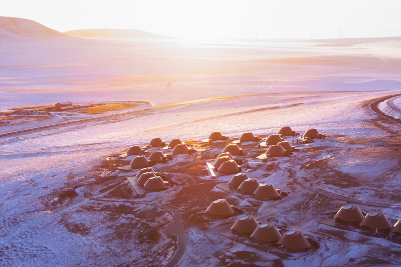 Oblique aerial view of dome shelters arranged in organic clusters across a snow-dusted plain at sunset