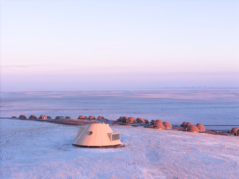 Single dome shelter with porthole window and rectangular opening standing in snowfield at dawn