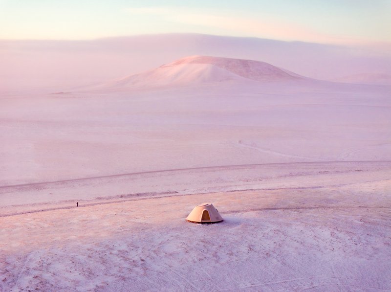 Solitary dome structure in foreground with distant figure and snow-covered hill in soft twilight