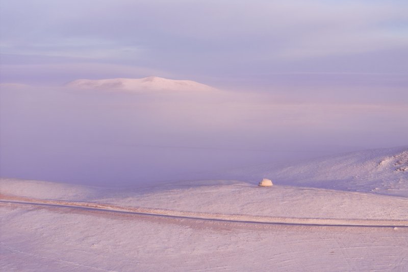 Dome shelter set in snowy valley with rolling hills and low cloud cover at dusk