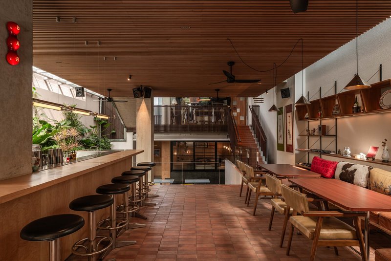 Open dining space with timber ceiling, long communal table, bar stools, and suspended pendant lights