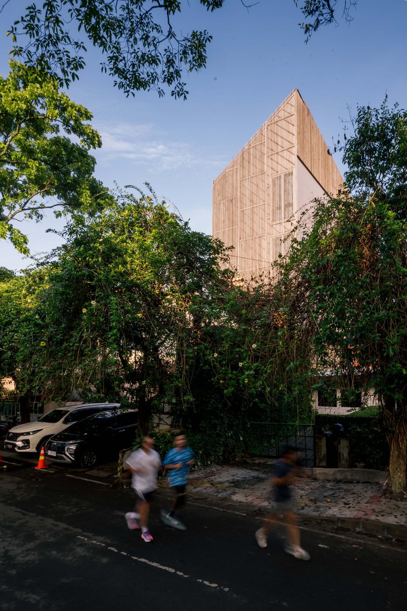 Timber-clad gabled volume rising above dense foliage with pedestrians crossing the street below