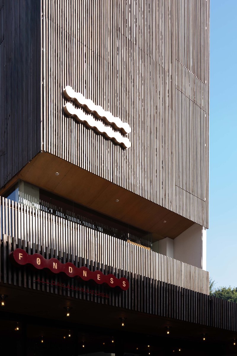 Vertically ribbed facade with a projecting canopy and illuminated signage against a clear blue sky