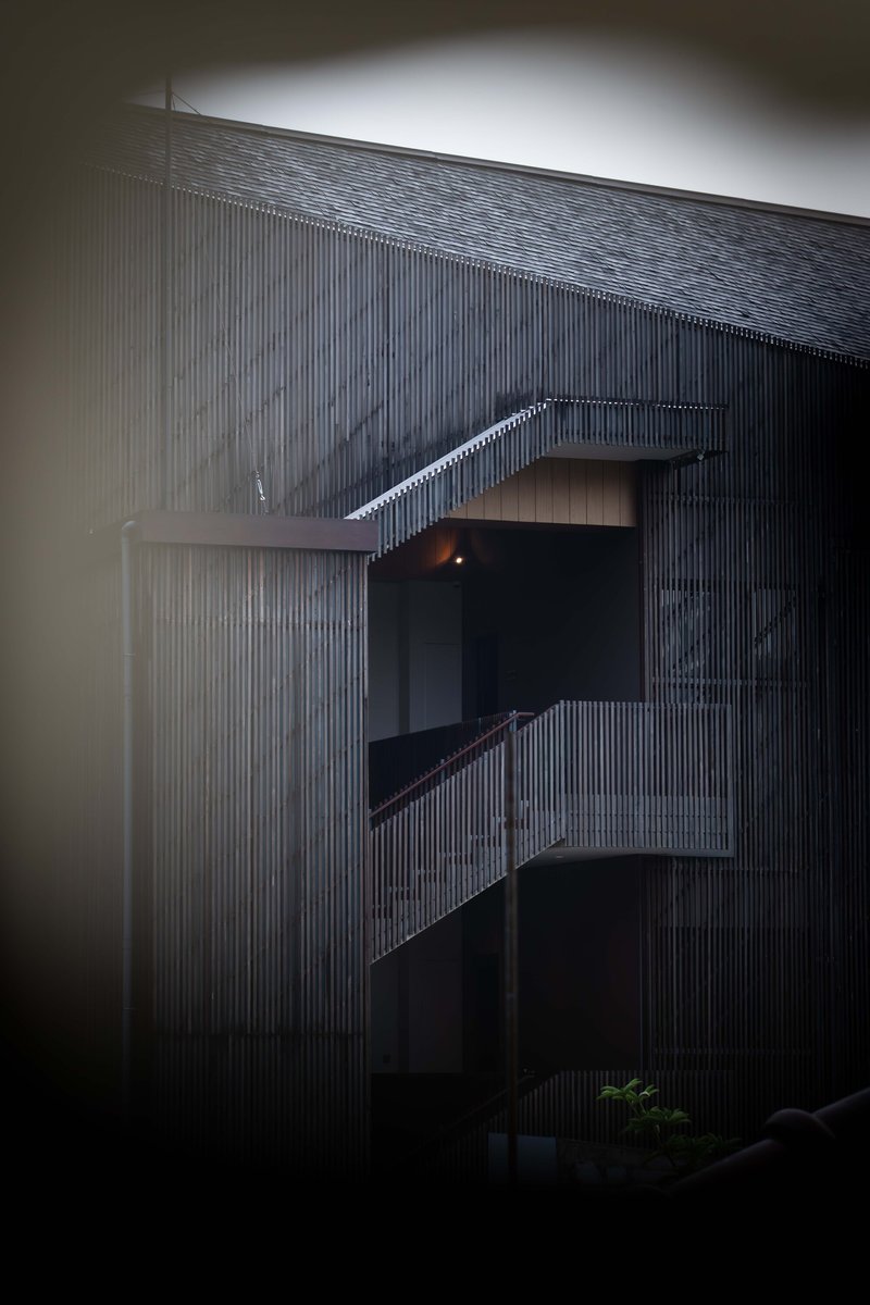 Exterior view of a cantilevered balcony with vertical slats and a curving wall in dim evening light