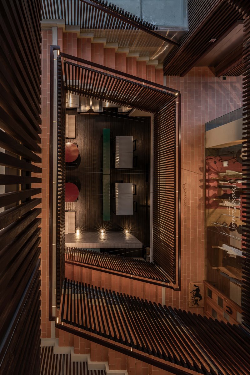 Vertical view into the stairwell showing terracotta floor tiles and slatted timber screens at dusk