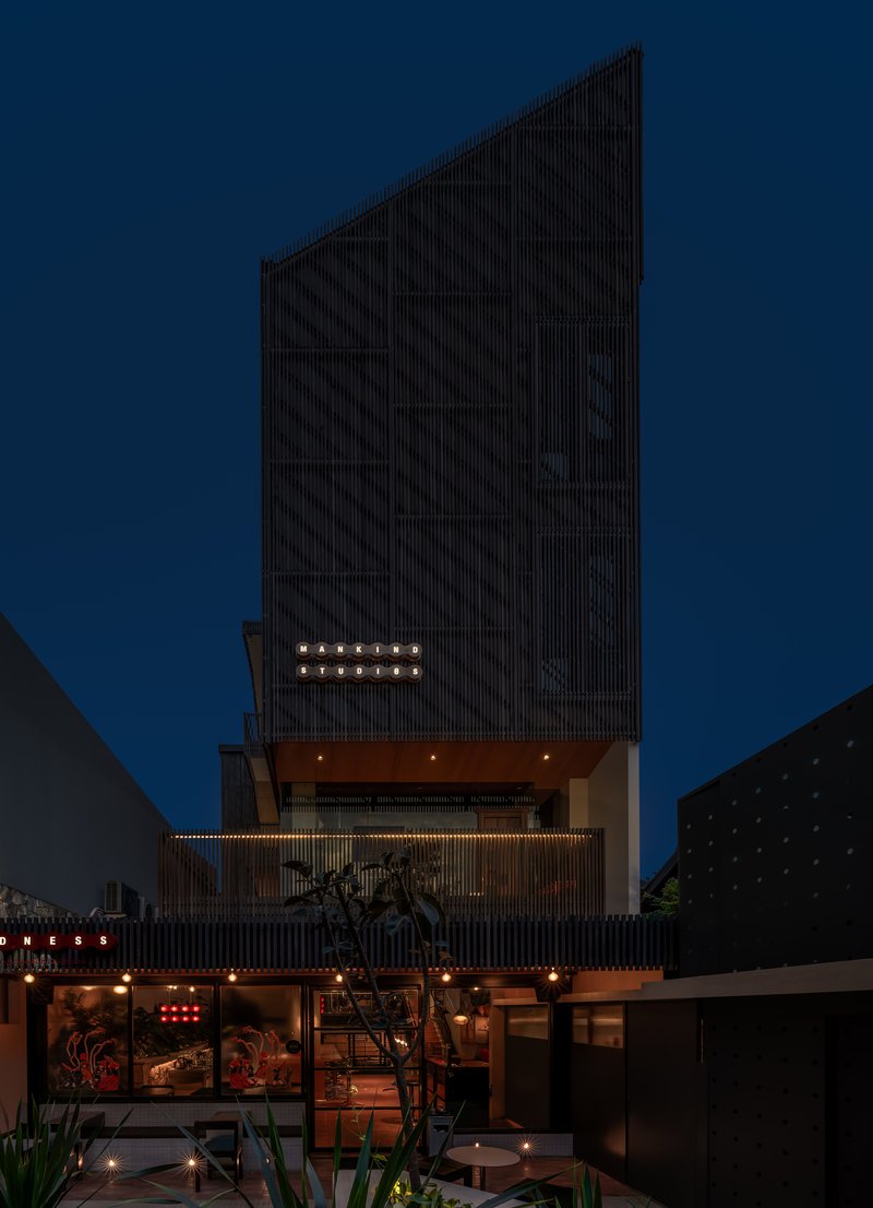 Night view of the facade with vertical slats, recessed balconies and string lights against a deep blue sky