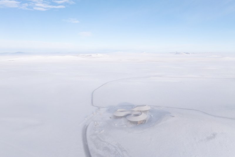 Drone view of the curving cloverleaf-shaped roof in a vast snowfield