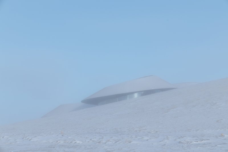 Single curved roof poking out of the snow under a clear blue sky