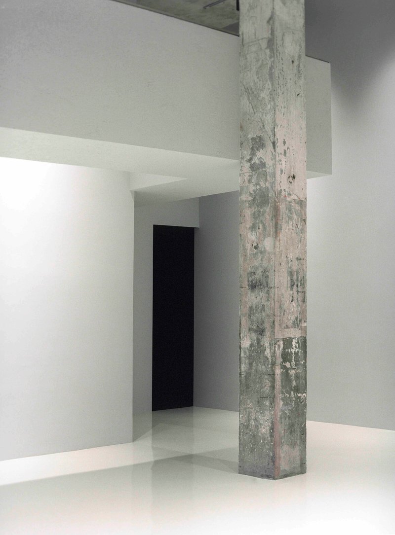Exposed concrete column standing in a white gallery space with smooth resin flooring