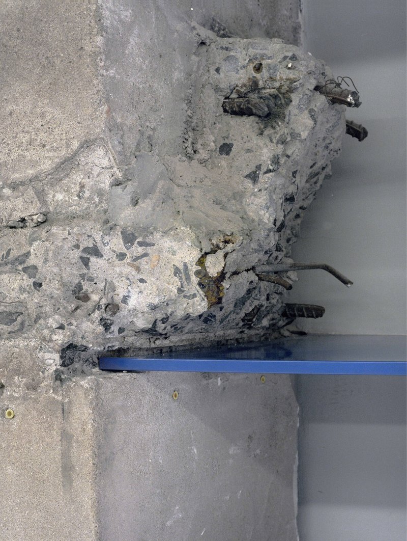 Close-up detail of deteriorated concrete with exposed aggregate and embedded metal reinforcement bars