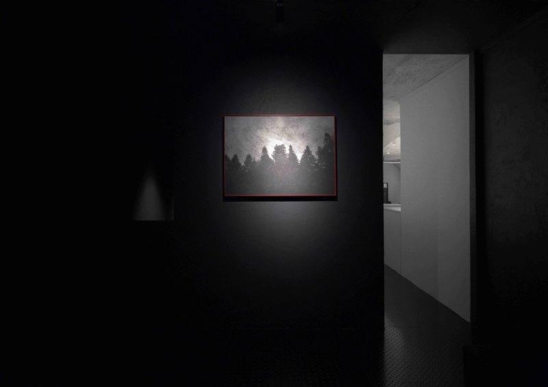 Gallery room with black walls and a single illuminated artwork beside an open doorway