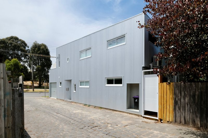 Side elevation with corrugated metal panels and a timber fence adjacent to the cobblestone lane