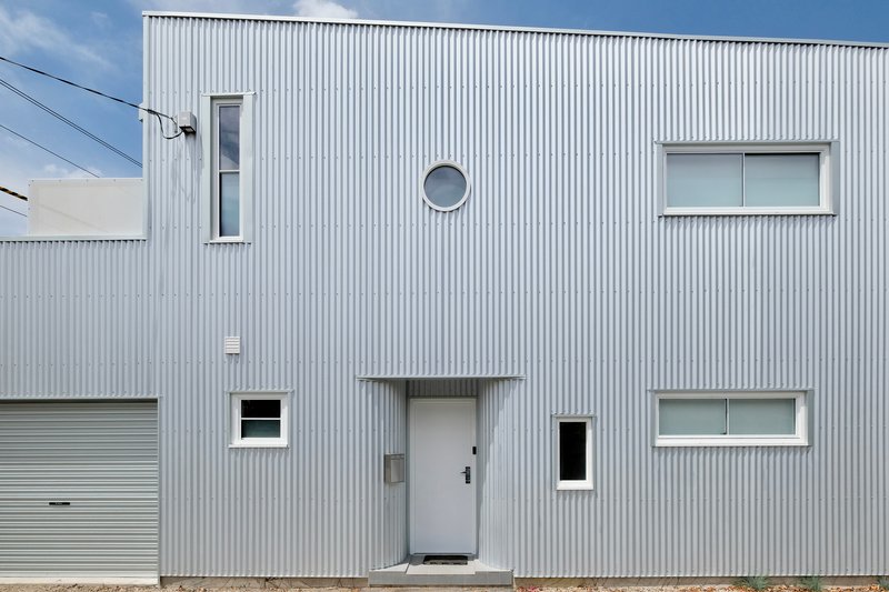 Front facade featuring a central door, circular porthole window, and scattered rectangular openings in corrugated cladding