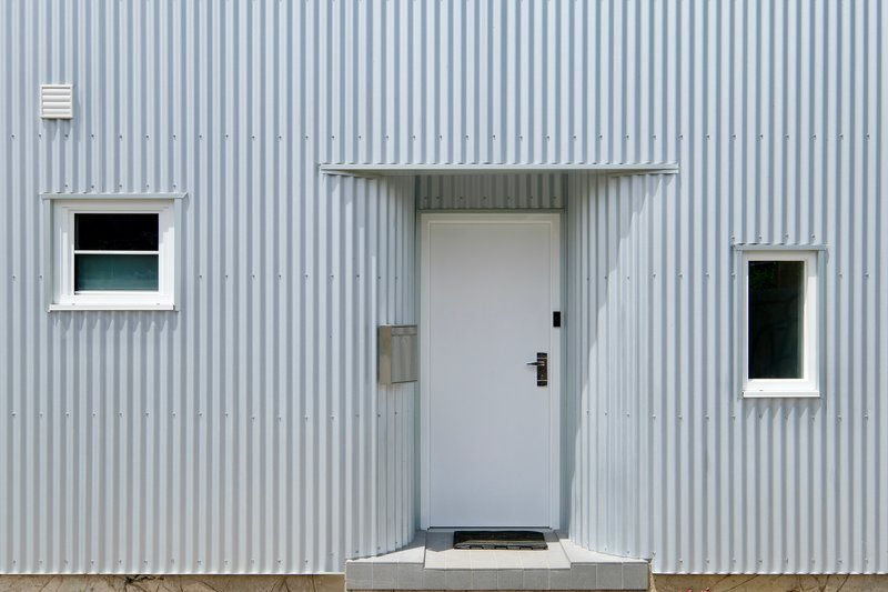 Close-up of the entry door flanked by two square windows on the ribbed metal wall