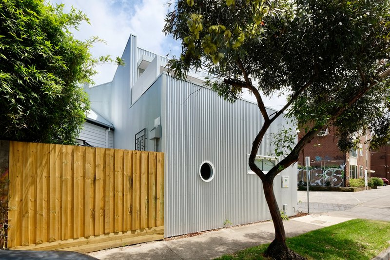 Rear view showing the corrugated facade behind a timber fence and an overhanging eucalyptus tree