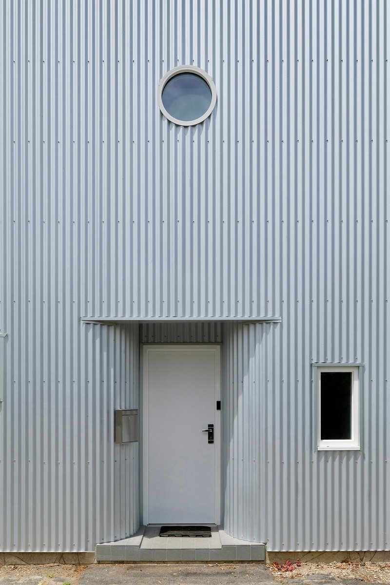 Entry door with canopy and circular porthole window set in the ribbed metal wall