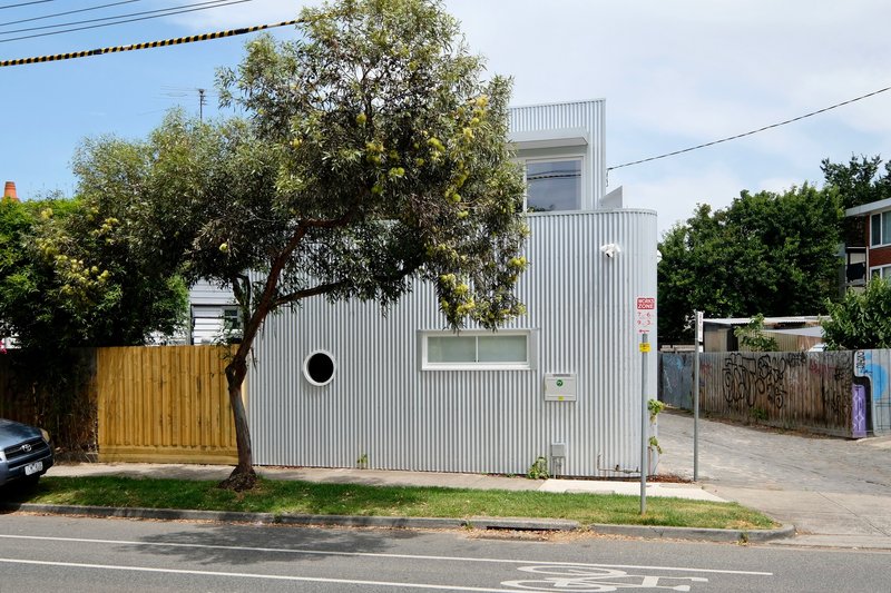 Side facade with circular window and horizontal slot opening beside a mature tree