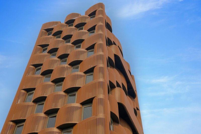Tower facade clad in vertical terracotta fins with undulating corner geometry against wispy clouds