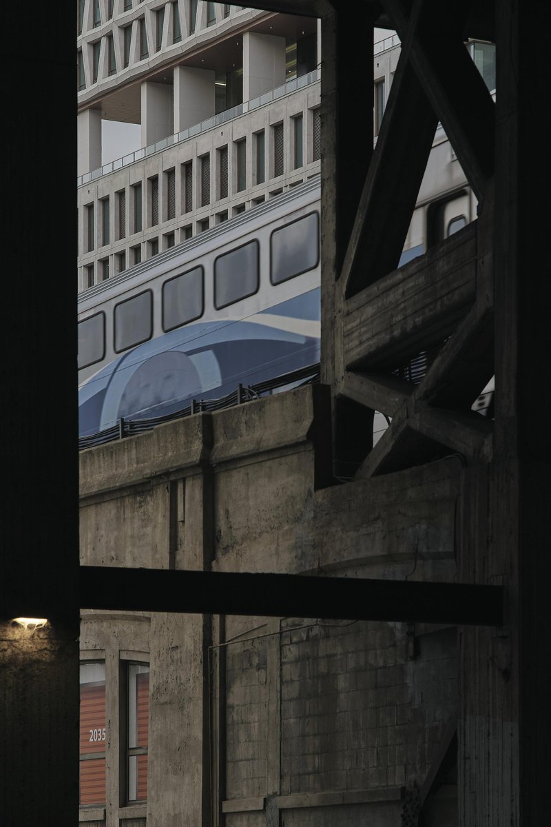 View through window openings showing layered concrete facades and an elevated transit guideway in shadow