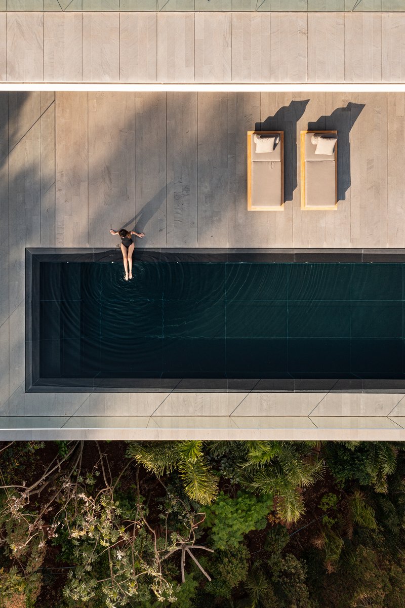 Top-down view of cantilevered pool deck with swimmer at the edge above treetops