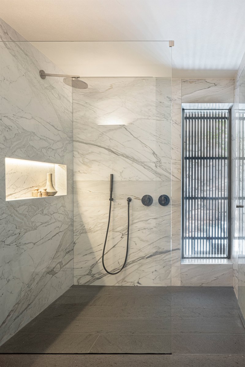 Bathroom shower enclosure clad in white marble with recessed niche and vertical louvered window