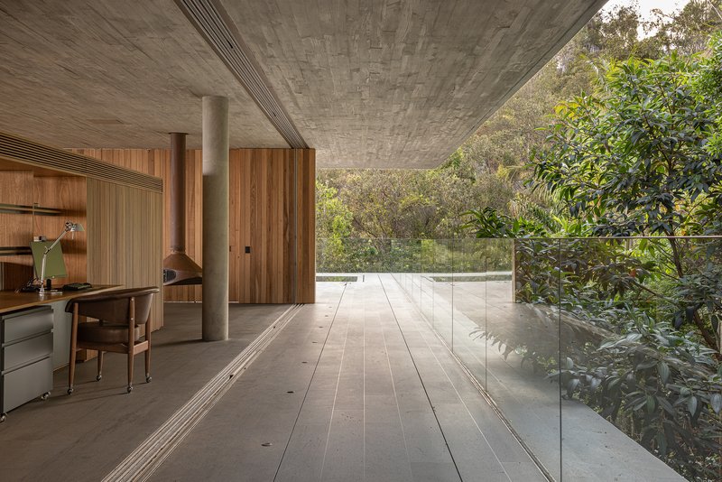 Glass-walled corridor with concrete ceiling and timber workstation opening to treetops