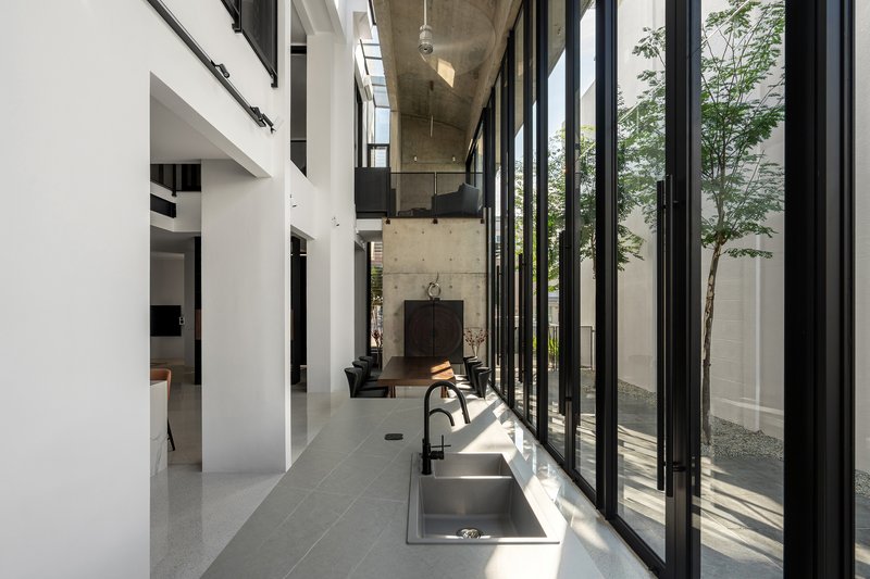 Interior corridor with terrazzo floor and folding glazed doors opening to a planted courtyard in sunlight